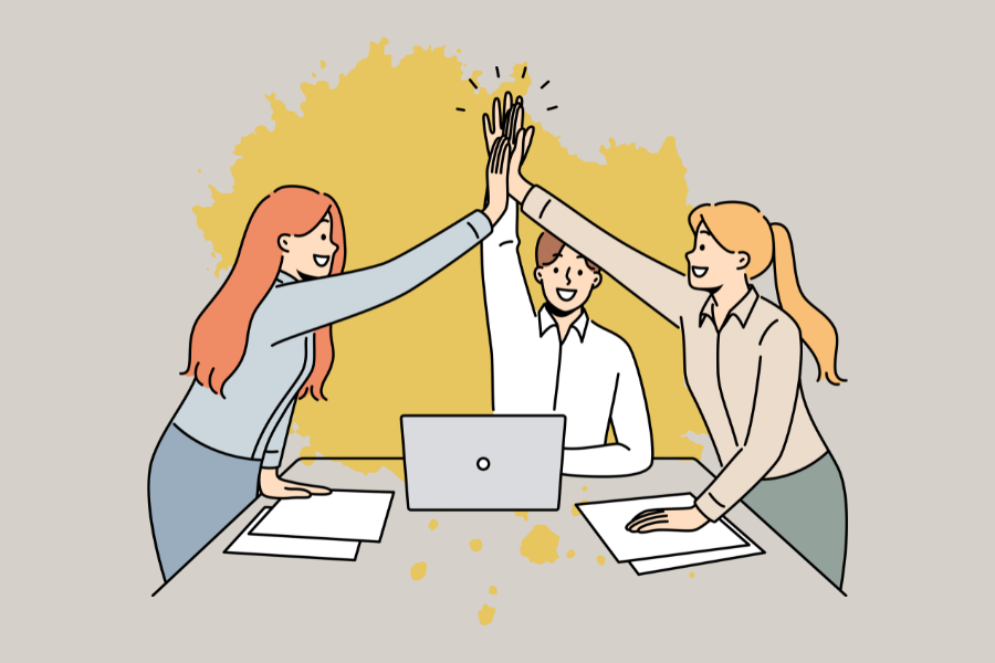 Illustration of 3 people at desk with papers and a laptop. They are high fiving to celebrate reaching completing their work.